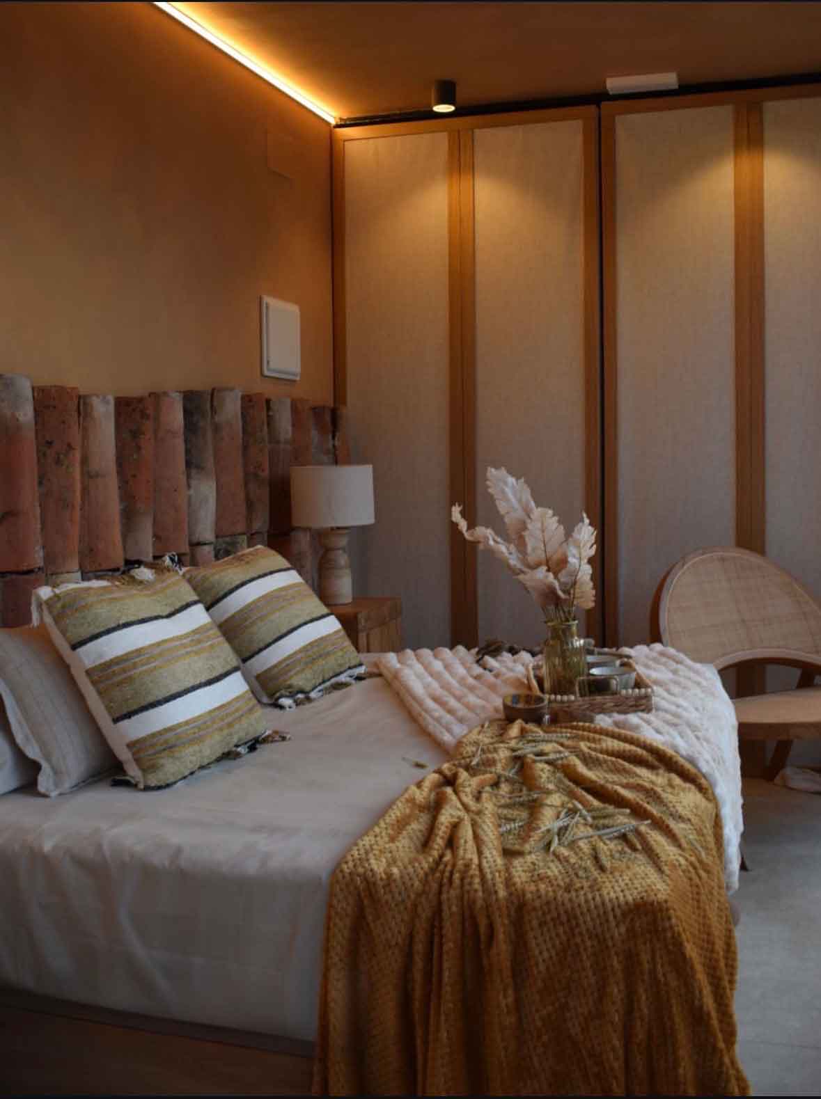 dormitorio wabi-sabi con cama de lino, cabecero de ladrillo recuperado y luz cálida en suite de teca y piedra en Burgos